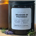 Black candle jar labeled 'Meadow in Provence' with lavender and rosemary on a wooden surface.